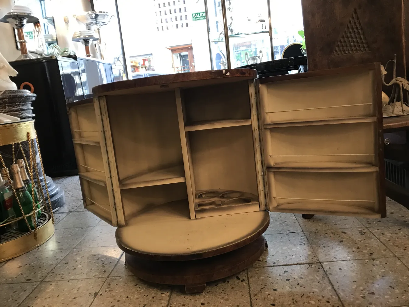 Mobile bar antico con porte che si aprono su un compartimento interno, elegante e funzionale, circondato da oggetti decorativi.