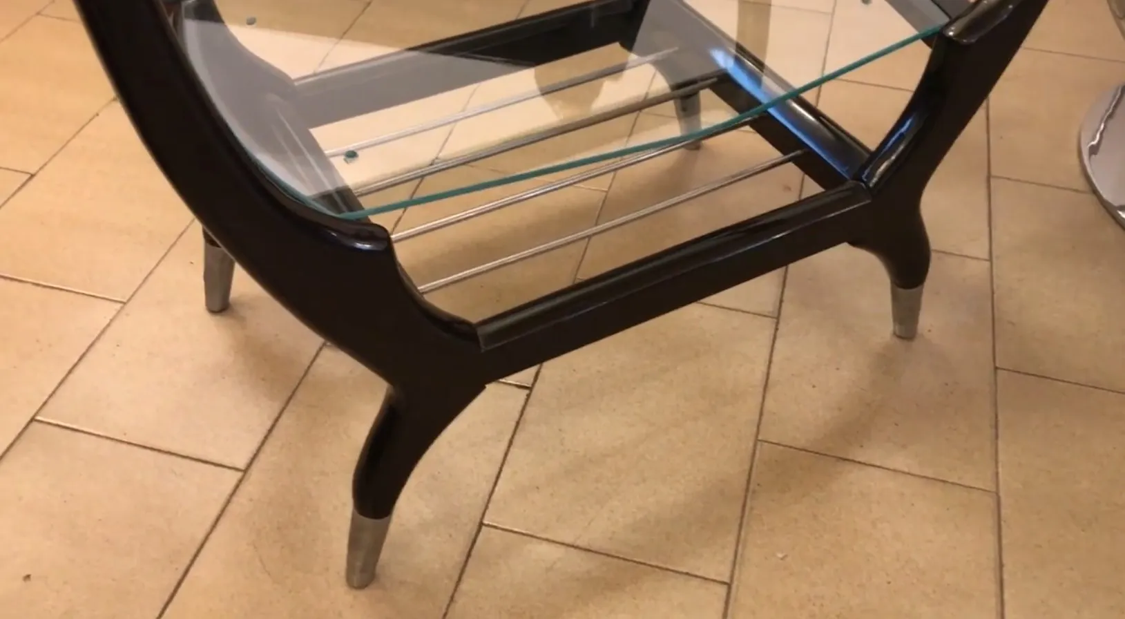 Mobile bar antico con piano in vetro e gambe eleganti in un contesto accogliente.