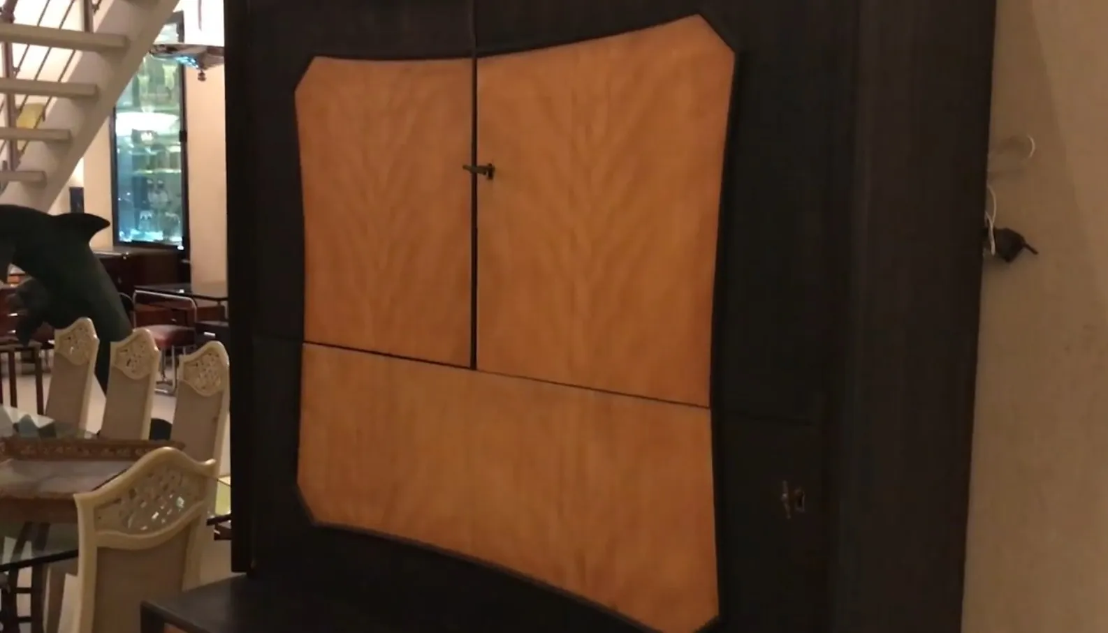 Meuble à cocktail antique avec un design élégant, finition lisse, dans un environnement confortable avec des chaises et un poisson en arrière-plan.