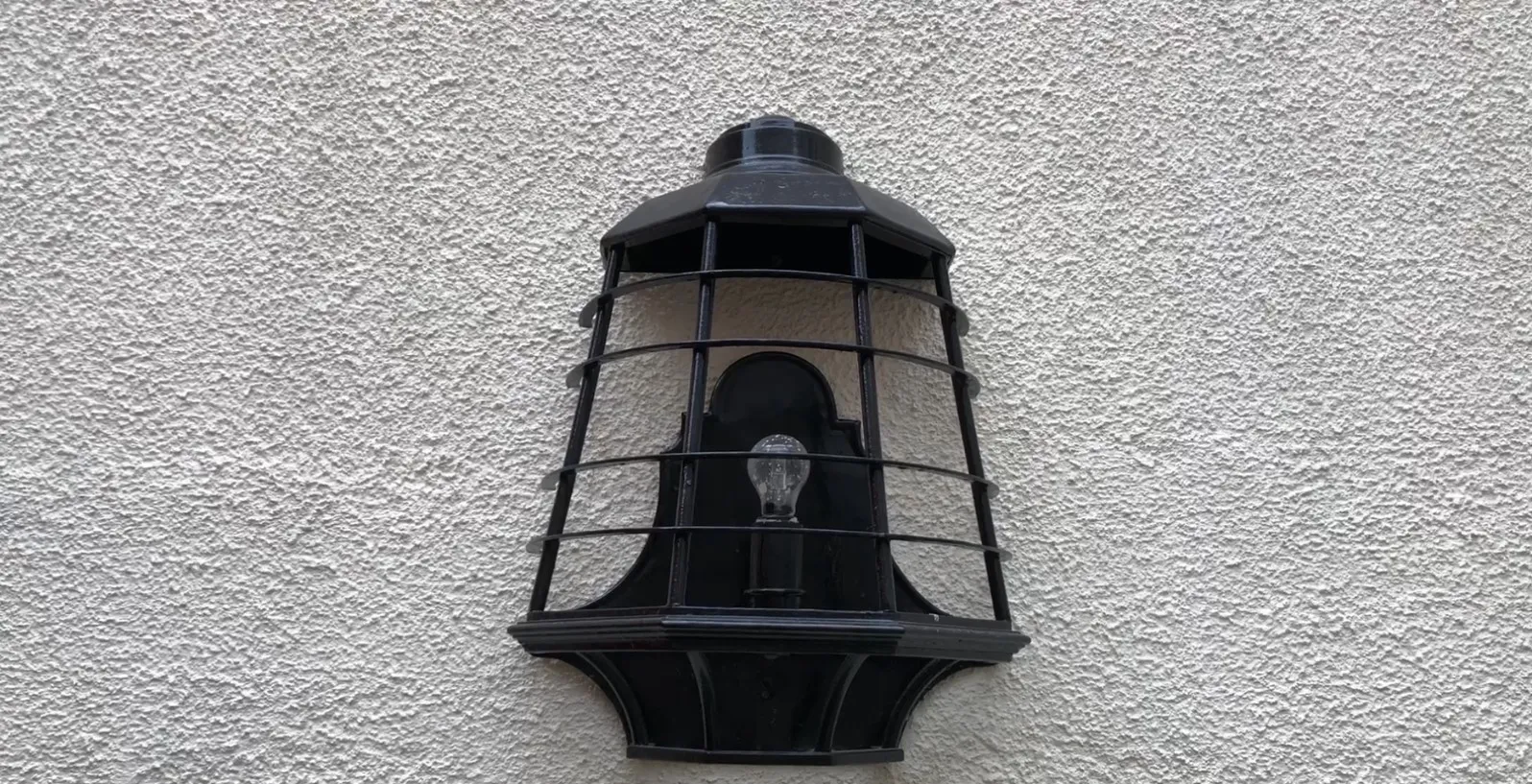 Paire d'appliques anciennes noires avec grille et ampoule sur mur blanc