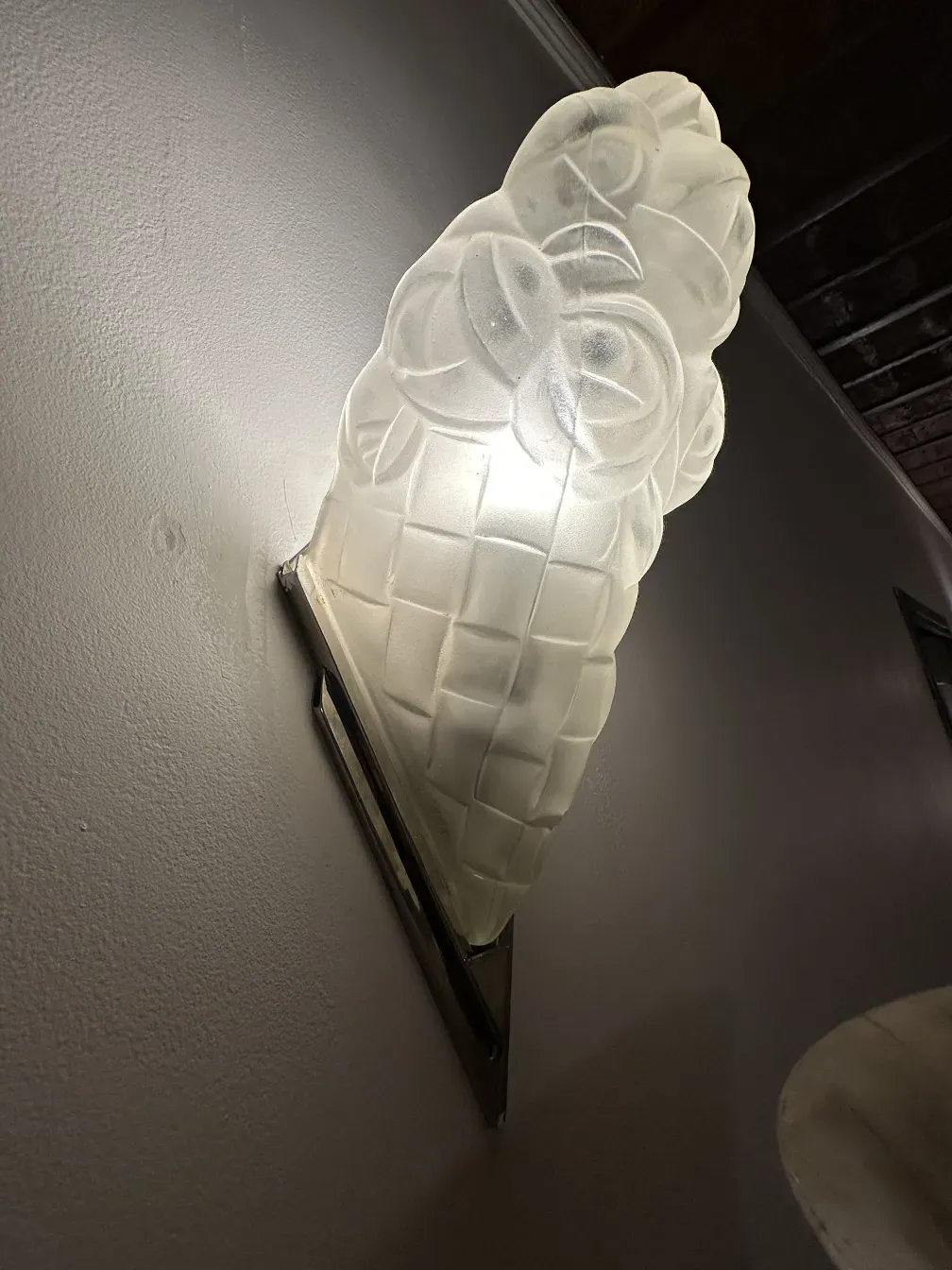 Applique antiche a forma di fiore con luce brillante su una parete chiara accanto a uno sfondo in legno.