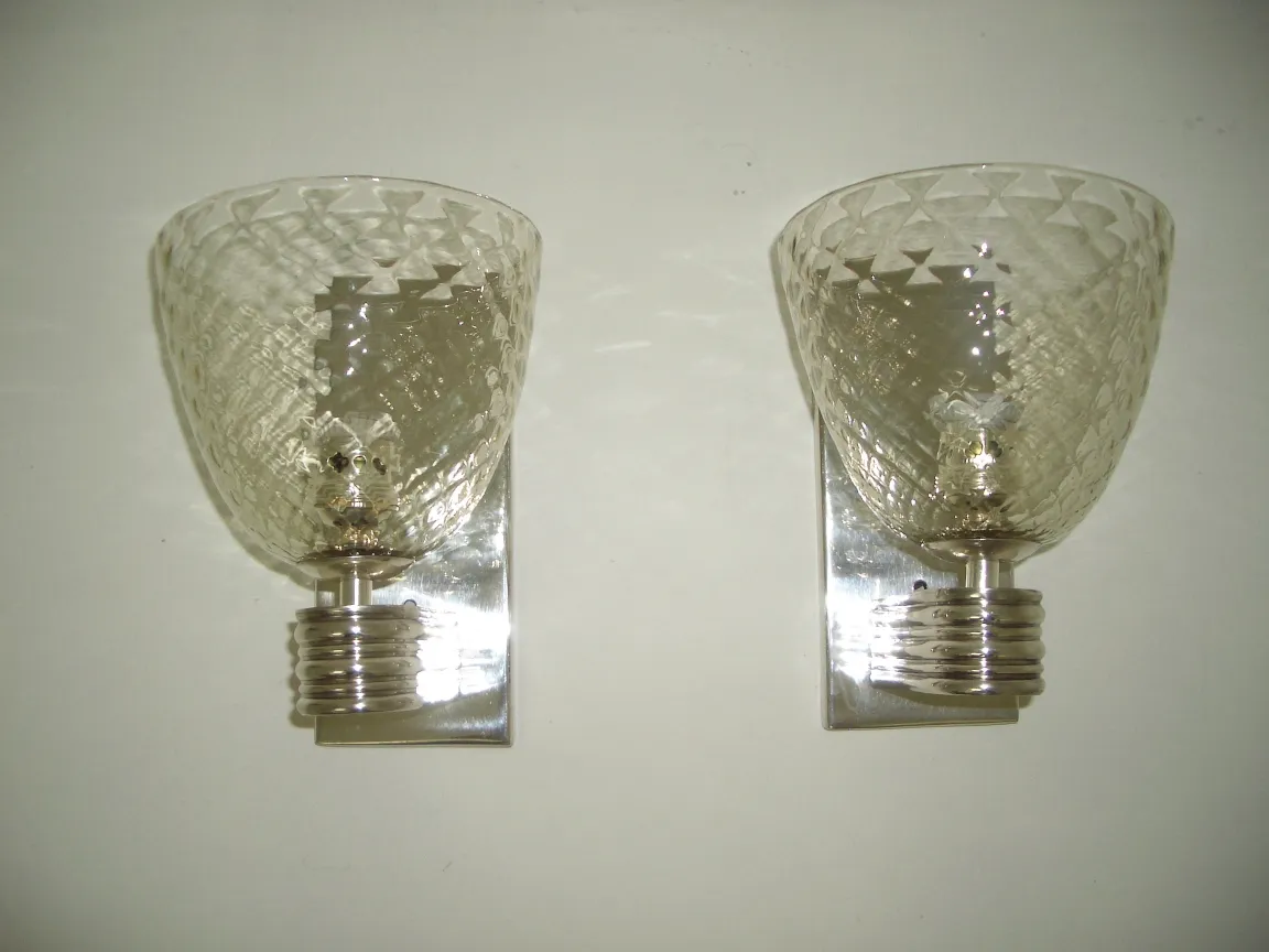 Par de apliques antiguos de cristal, con una base metálica brillante, colocados en una pared blanca.