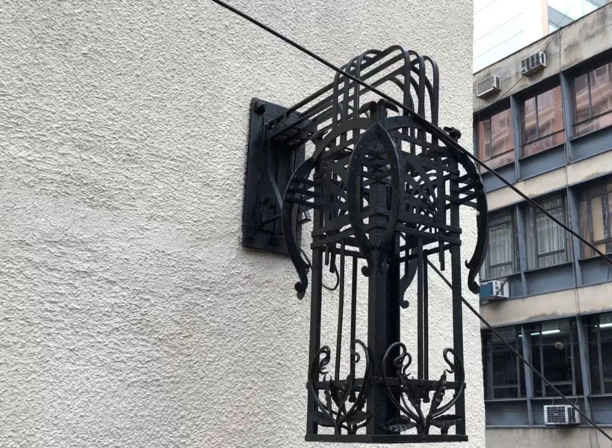 Antiguo par de apliques con diseño elegante en color negro, montados en una pared clara, rodeados de un ambiente urbano.