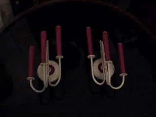 Paire d'appliques anciennes avec bras courbes et bougies roses, éclairant un cadre sombre.