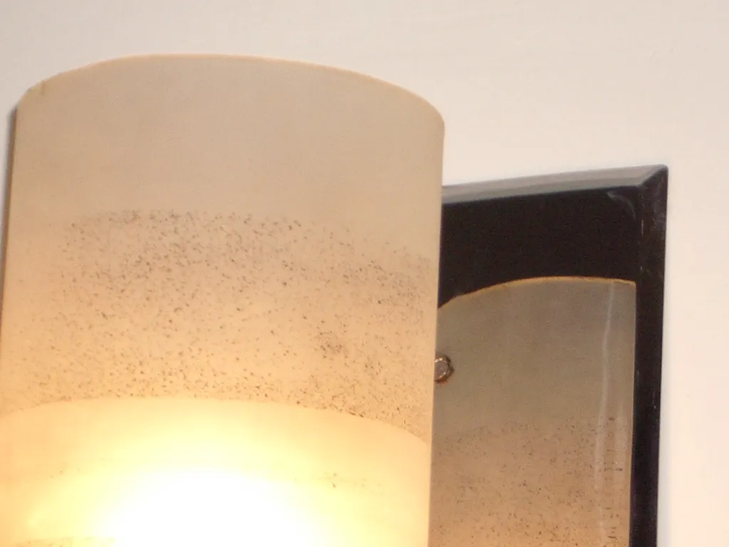 Par de luminárias de parede antigas com telas difusas iluminando uma parede branca.