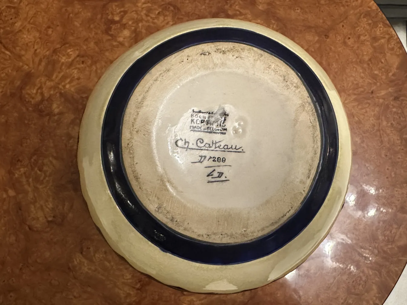 Plat en céramique ancienne avec un bord bleu sur fond blanc.