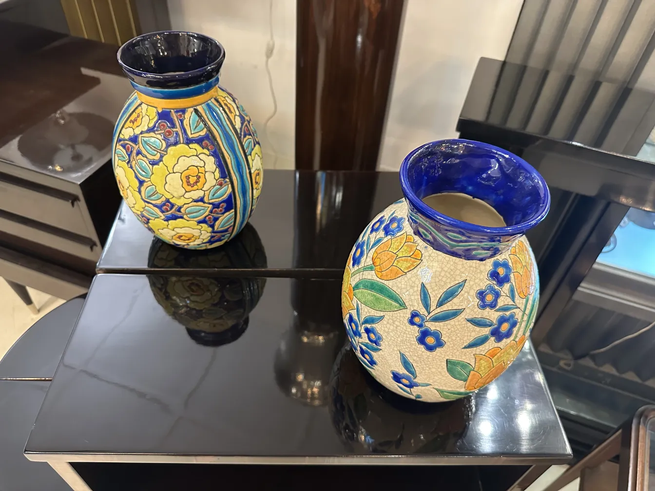 Deux vases en céramique antiques avec des motifs floraux et des couleurs vives sur une table noire.