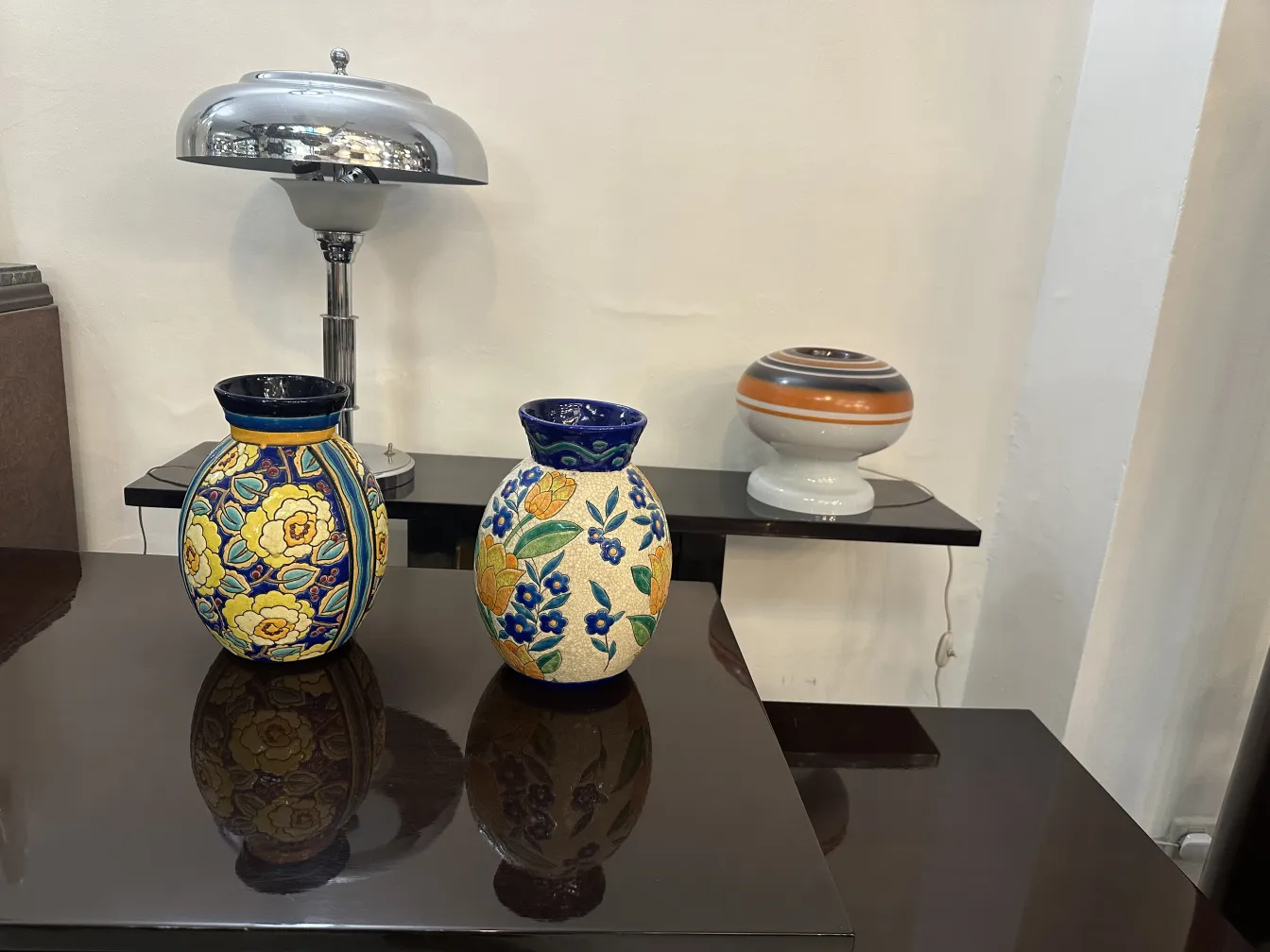 Dos jarrones de cerámica antigua con decoración floral, sobre una mesa oscura, con una lámpara moderna de fondo.