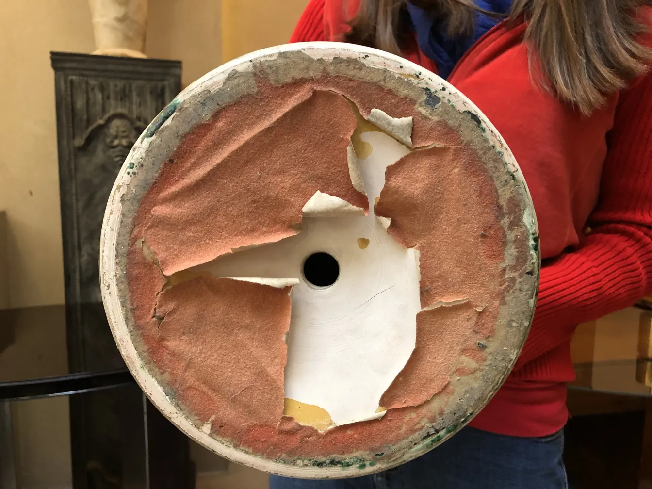 Visão inferior de uma cerâmica antiga com base danificada, cercada por um ambiente acolhedor.