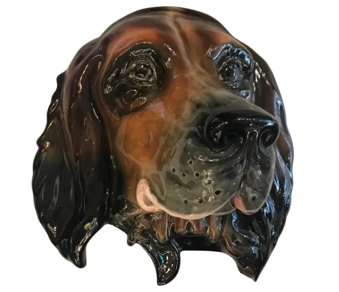 Escultura antigua de cerámica en forma de cabeza de perro con colores marrones y negros.