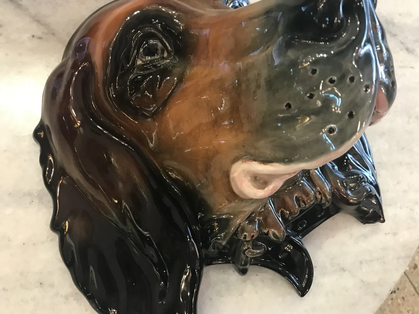 Escultura antigua de un perro en cerámica, con detalles de color marrón y negro.