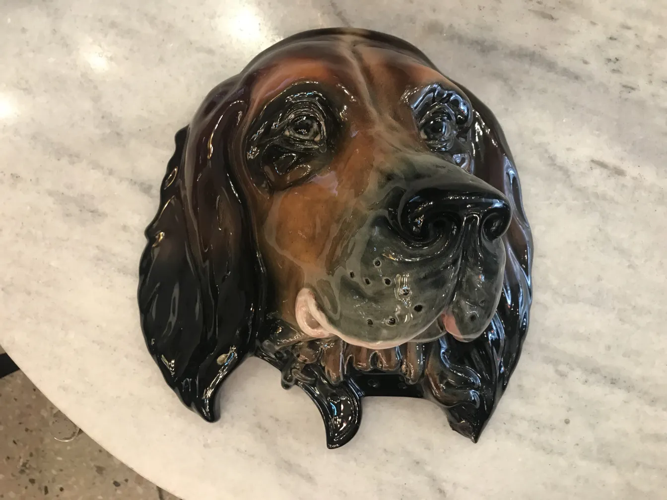 Escultura de cerámica antigua en forma de perro, brillante y detallada, sobre una superficie clara.