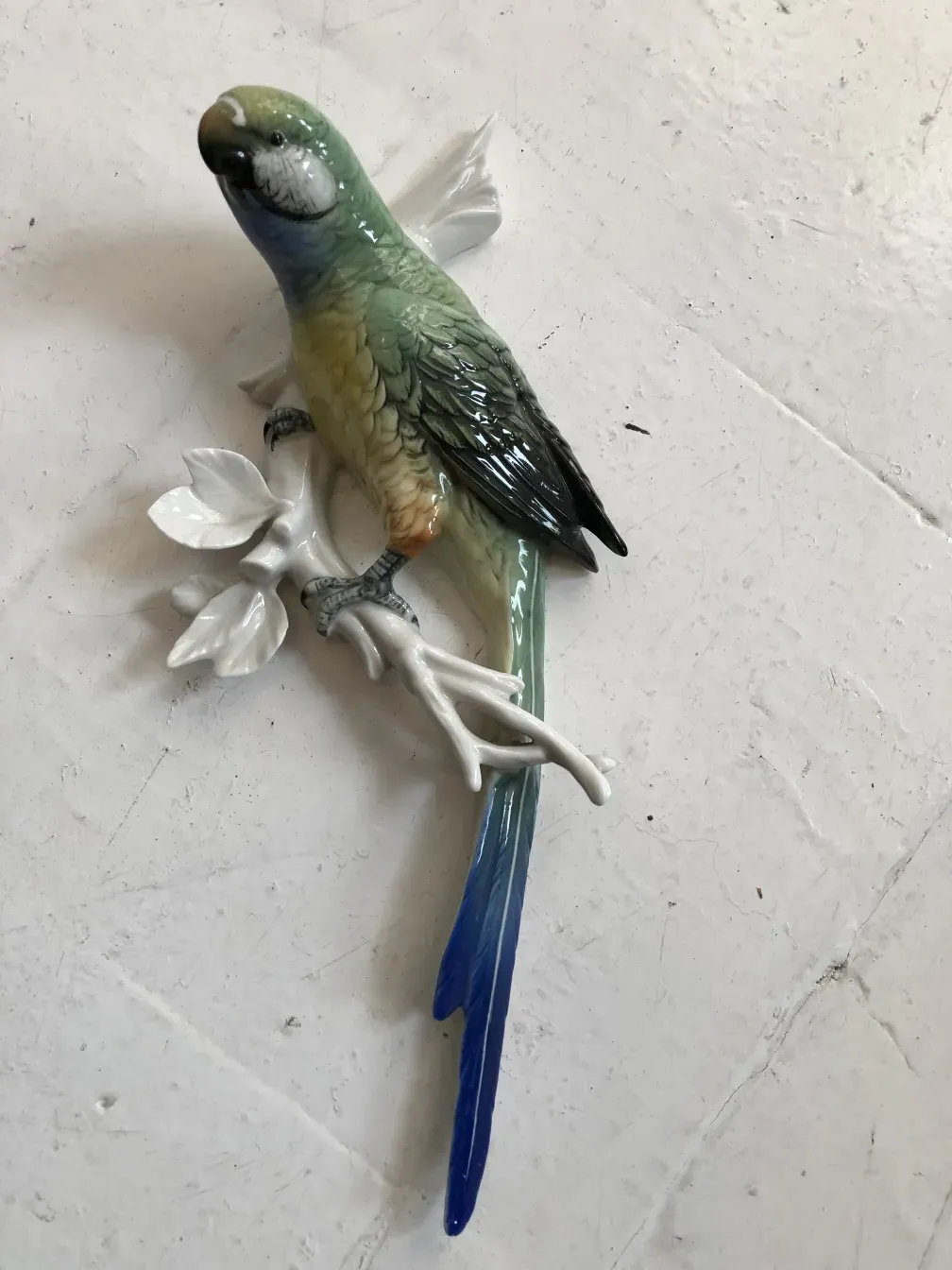 Antiga figura de cerâmica de um pássaro colorido em um galho branco.