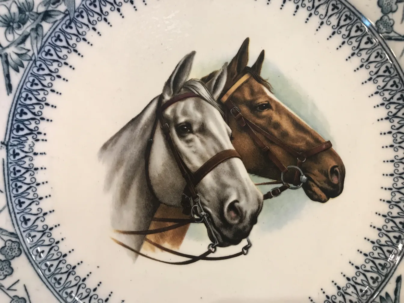 Antique ceramic plate featuring two realistic horses, one gray and one brown, with a decorative border.