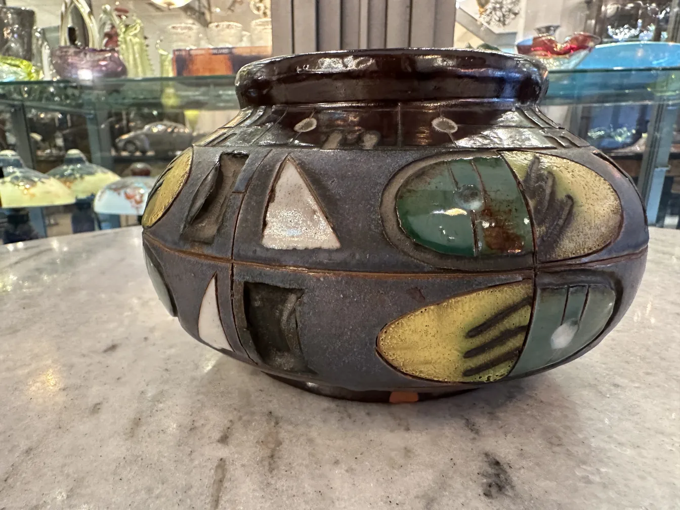 カラフルなデザインの古い陶器の花瓶、背後に展示棚。