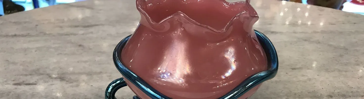 Vase en verre rose avec un bord bleu et un design artistique.